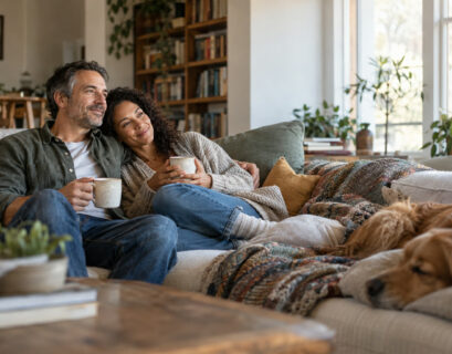 Middle-aged couple sitting close on a sofa at home sharing morning coffee in soft daylight